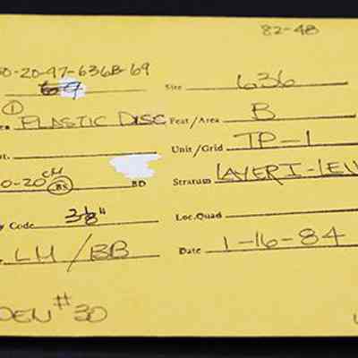 Artifact envelope for plastic disc: The image shows a yellow envelope with handwritten notes, detailing excavation information such as date, specimen type, depth, recovery code, and location.