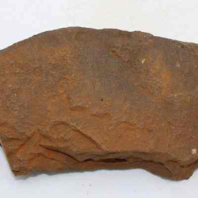 Top view of whetstone (hoana) fragments placed together: The image shows a rough, irregularly shaped fragment of a whetstone (hoana) with a brownish surface, likely used historically for sharpening tools or blades.