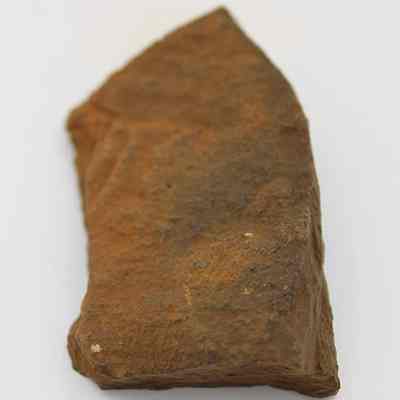 Lengthwise view of whetstone (hoana) fragments placed together: The image displays a rough, uneven fragment of a whetstone (hoana) with a slightly pointed shape and a natural, earthy brown color, indicating wear and historical use.