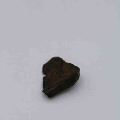 Closeup of basaltic glass flake: A small, dark basaltic glass flake with a rugged texture is set against a smooth, plain background.