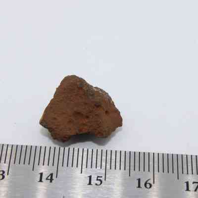 Closeup of basaltic glass core and ruler: The image shows a small, reddish basaltic glass core on a white surface with a ruler indicating its size.