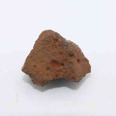 Closeup of basaltic glass core: The image shows a rough, brown basaltic glass core piece, displaying porous surface and irregular edges against a plain background.