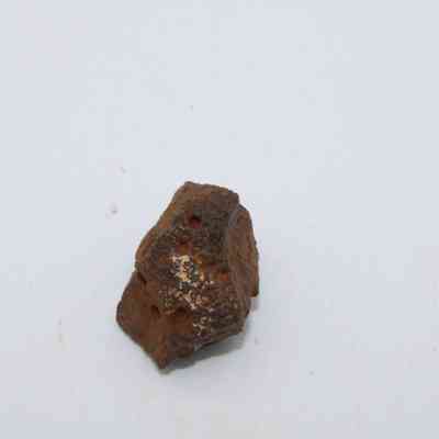 Closeup of basaltic glass core: The image shows a small, irregularly shaped piece of basaltic glass on a plain white background, displaying a rough texture and dark hue.