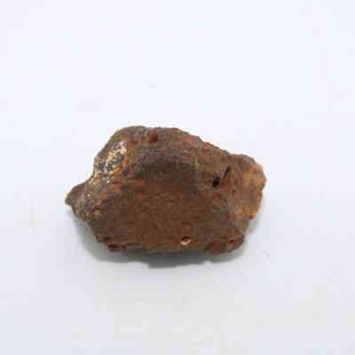 Closeup of basaltic glass core: The image shows a rough, irregularly-shaped piece of basaltic glass core, with a brown, porous surface against a plain white background.