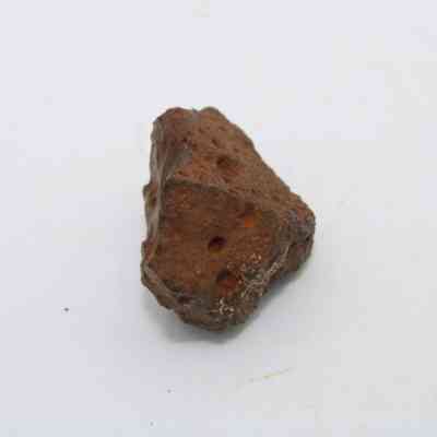 Closeup of basaltic glass core: The image shows a rough, angular piece of basaltic glass, featuring a reddish-brown hue and uneven surface with visible porous textures.