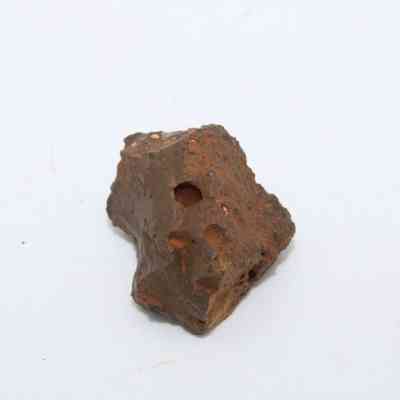 Closeup of basaltic glass core: The image displays a rough, irregularly shaped piece of basaltic glass core, showcasing a dark, earthy texture and noticeable surface indentations.