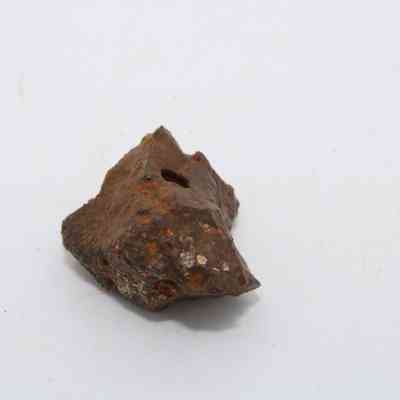 Closeup of basaltic glass core: A rugged, dark piece of basaltic glass core rests on a plain white background, showcasing its rough texture.