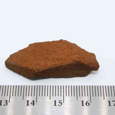 Closeup of basaltic glass flake with metal ruler: The image shows a small, rough basaltic glass flake placed next to a ruler for scale measurement purposes.