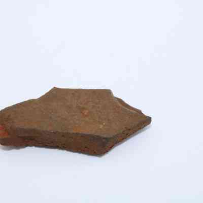 Closeup of small basaltic glass flake: A single piece of basaltic glass flake lies on a plain white background, showcasing its natural, irregular shape and earthy coloration.