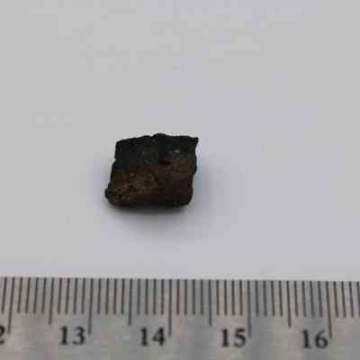 Close up of basaltic glass flake with ruler: The image shows a small basaltic glass flake placed next to a ruler, highlighting its size against a plain white background.