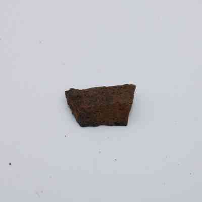 Basaltic glass flake: The image shows a basaltic glass flake with a rough, dark texture, resting on a plain white background, highlighting its natural formation.