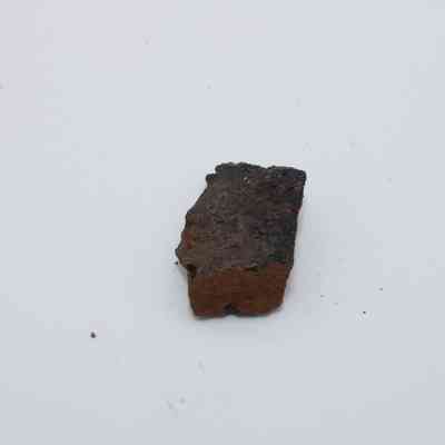 Basaltic glass flake: The image shows a small, rough basaltic glass flake with a dark, uneven surface, positioned against a plain, white background.