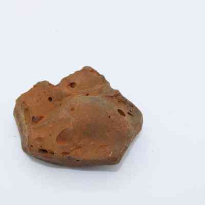 Closeup of basaltic glass core: The image displays a fragment of basaltic glass with a rough surface and various small holes against a plain white background.