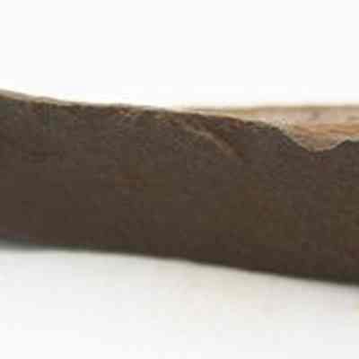 Profile of a basalt awl: The image shows a pointed, brown stone tool, resembling an ancient awl, with a rugged surface suitable for piercing or drilling materials.