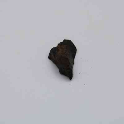 Basaltic glass flake: A small piece of basaltic glass flake lies on a plain white surface, showcasing its dark, rough texture and angular shape.