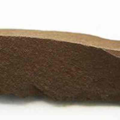 Profile of a basalt awl: The image shows a rough, brown stone tool awl, with a sharp edge and uneven surfaces, likely used in ancient times for piercing or drilling.