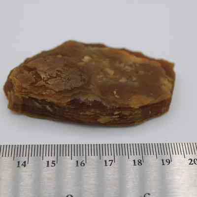 Closeup of agate flake above a metal ruler: The image shows a brown agate flake with visible layers, placed next to a metal ruler showing centimeters for scale.