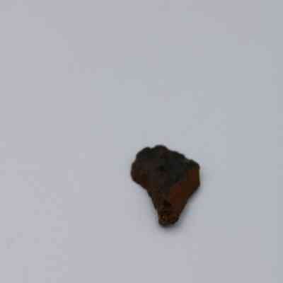 Closeup of basaltic glass flake: A small flake of basaltic glass rests on a plain white surface, showcasing its dark, slightly rough texture.