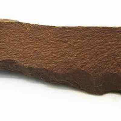 Profile of basalt awl: The image shows an awl made of brown stone, displaying a rough, uneven surface with a pointed tip and a broad base.