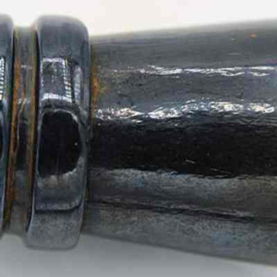 Closeup of glass bottle fragment (mouth and neck): The image shows a glossy, dark glass bottle fragment with a cylindrical shape, featuring a thickened upper portion and a tapered break at the bottom edge.