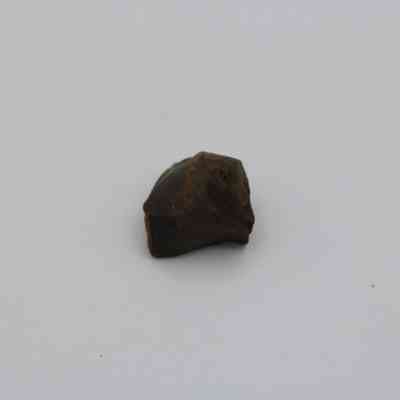 Glass core: The image shows a small, dark brown glass core with an irregular, rough surface, placed against a plain white background.