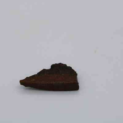 Closeup of small basaltic glass flake: The image shows a small, dark brown basaltic glass flake lying on a light, flat surface with distinct edges.