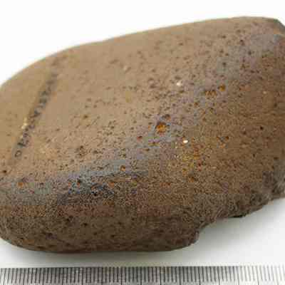A basalt hammerstone with a ruler: The image shows a rough, brown stone with an irregular shape and texture, placed on a flat surface, and a ruler beside it for scale.