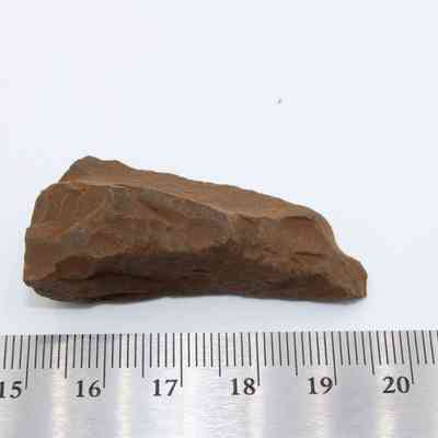 Closeup of possible auger with ruler: The image shows a roughly hewn, brown stone artifact placed next to a ruler for scale, suggesting it might be a tool or auger.