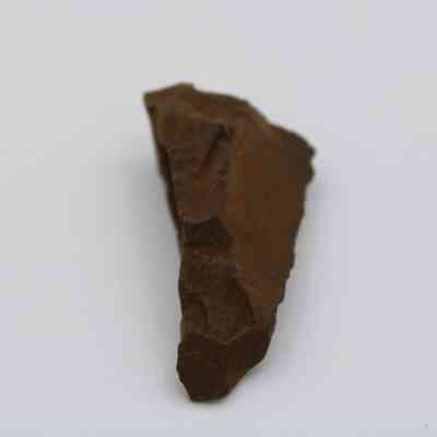 Lengthwise of possible auger: The image shows a rust-colored, primitive stone tool with sharp, jagged edges resembling an auger against a white background.