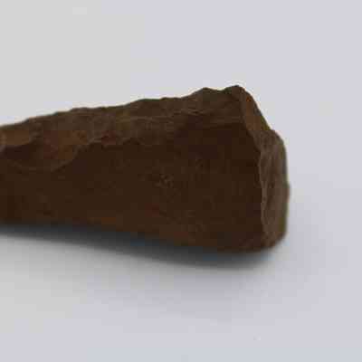 Profile of a possible auger: The image shows a rough, brown stone tool with sharp edges, possibly used historically as an auger for drilling or cutting purposes.