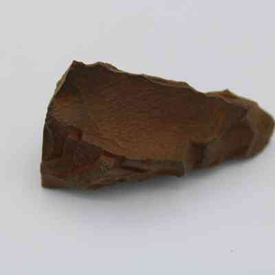 Profile of possible auger: The image shows a pointed, jagged stone artifact resembling an ancient tool, possibly an auger, with a reddish-brown hue.