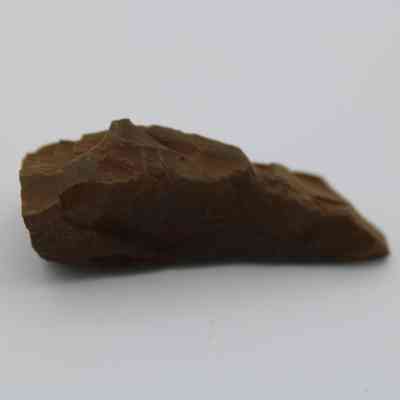 Profile of possible auger: The image shows a roughly shaped, brown, stone tool or fragment, possibly an ancient auger, resting on a plain white background.
