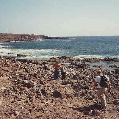 Three people walking along rocky shoreline