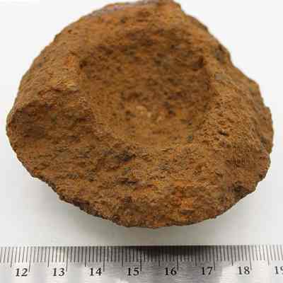 Broken cup or mortar with ruler: This image shows a small, rough-textured stone object with a bowl-shaped indentation, possibly used as a mortar for grinding substances.