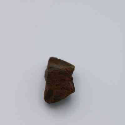 Closeup of basaltic glass core: The image shows a small piece of basaltic glass core with a rough, dark surface set against a plain, light background.