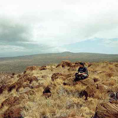 Unidentified person sitting on a pohaku (boulder)
