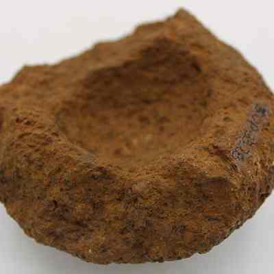 Closeup of broken cup or mortar with alternate id number visible: The image shows a rough, stone object that resembles an ancient mortar, with a shallow, rounded indentation in the center and a textured, weathered surface.