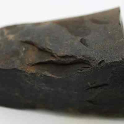 Close up of basalt adze fragment: The image shows a fragment of an adze, made of dark stone, with a rough and uneven surface.