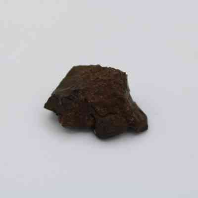 Closeup of a glass core: The image shows a rough, dark glass core with an irregular shape, lying on a plain white background.