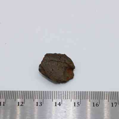 Closeup of glass flake with ruler: A small, irregularly shaped glass flake is placed on a flat surface next to a metallic ruler for scale and measurement.