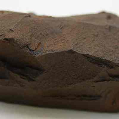 Closeup profile of basalt adze blank: The image shows a rough, dark brown adze blank with sharp edges and a textured surface, lying on a flat, white background.
