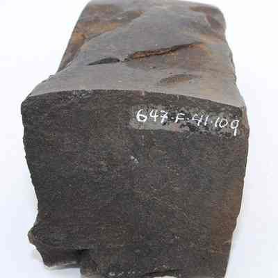End of basalt adze fragment with original id number visible: This image shows a dark stone adze fragment with a rough surface, featuring chiseled edges and the number 647.F:41.109 written on one end.