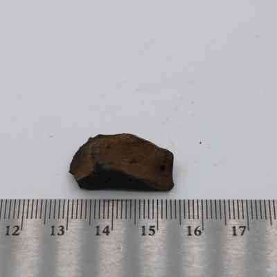 Closeup of basaltic glass flake with metal ruler: The image shows a small, rough basaltic glass flake next to a ruler, indicating its size is approximately 3 centimeters on a white background.