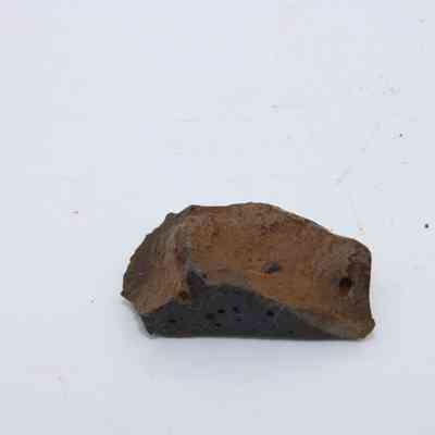 Closeup of basaltic glass flake profile: The image shows a single piece of basaltic glass flake with a rough, dark surface lying on a light background.