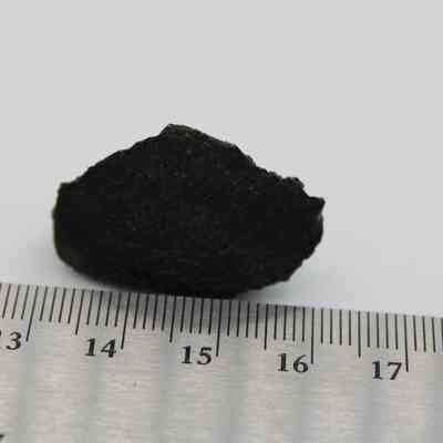 Closeup of basaltic glass flake with ruler: A dark, irregular-shaped basaltic glass flake is positioned beside a metric ruler, measuring approximately 3 centimeters.