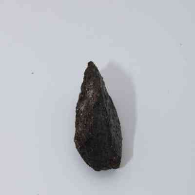 Top view of basaltic glass flake: The image depicts a dark, jagged basaltic glass flake with a rough texture, placed against a neutral background, highlighting its natural form.