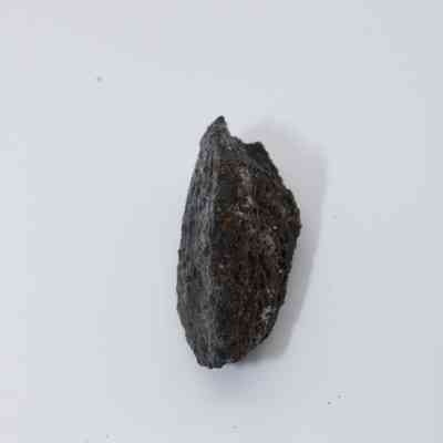 Top view of basaltic glass flake: A jagged piece of basaltic glass flake sits against a plain white background, showcasing its dark, textured surface and sharp, angular edges.