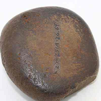 Close up of basalt hammerstone with visible alternate id number: The image shows a large, smooth, dark brown stone with some surface texture and a sequence of numbers written down its center.