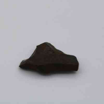 Profile of basaltic glass flake: The image depicts a dark, irregularly shaped basaltic glass flake resting on a plain white surface, highlighting its texture and natural formation.