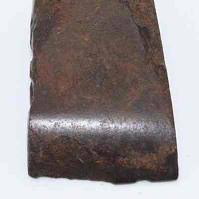 Lengthwise view of small basalt adze (ko'i) with ruler: The image depicts a small stone adze (ko'i) with a flat surface, situated against a plain background above a metric ruler for scale reference.